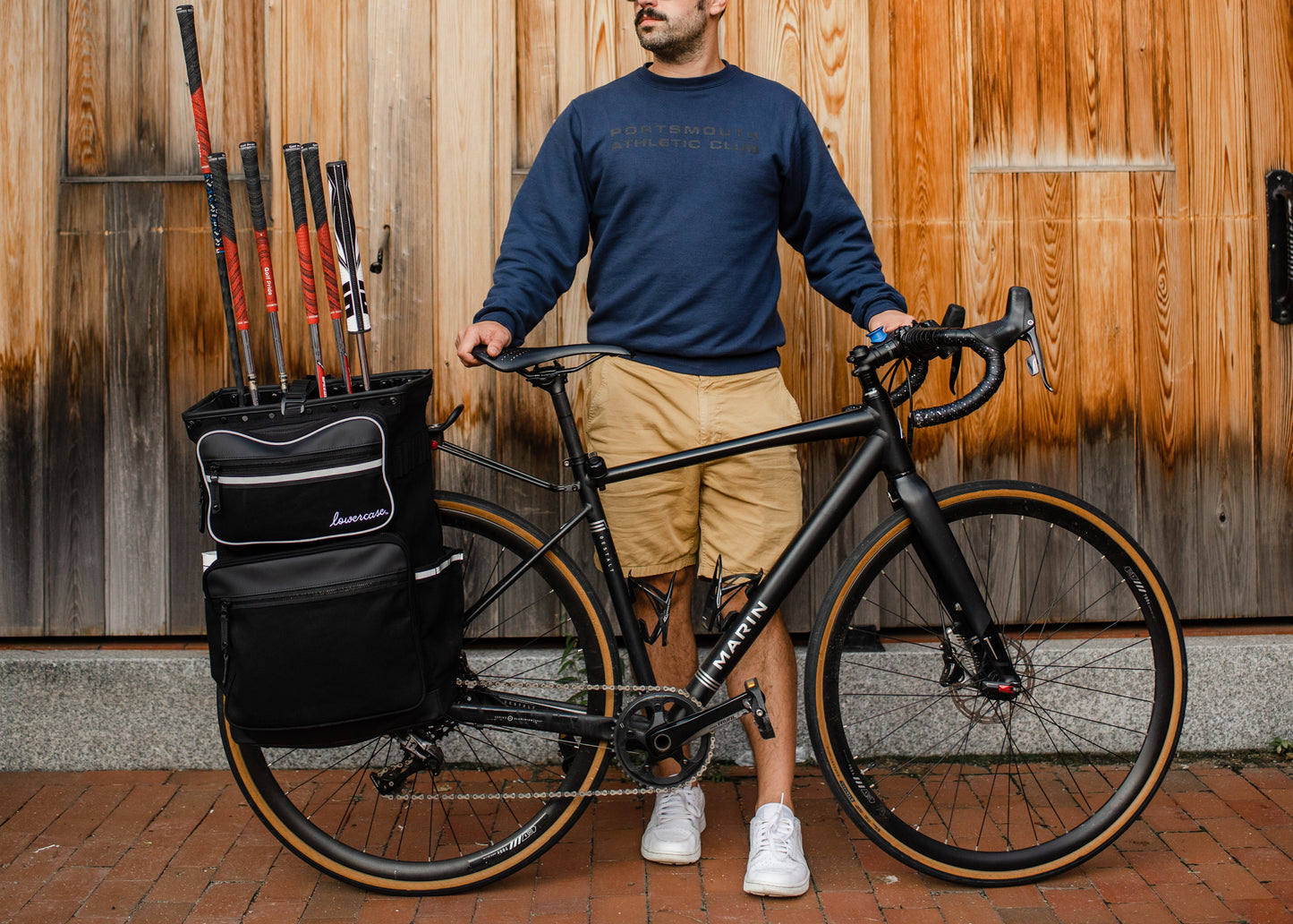 Man standing next to a bicycle with a pannier golf bag attached to the back of the bicycle.
