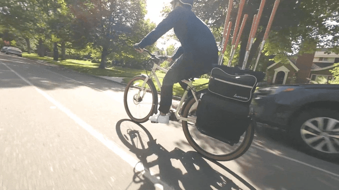 Person riding a bicycle with a golf backpack attached to bike on a sunny day.